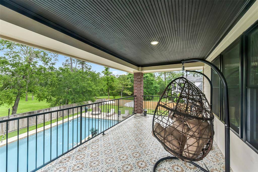 This photo showcases a covered balcony. It overlooks a spacious backyard with a swimming pool and lush greenery, offering a serene and inviting outdoor space.