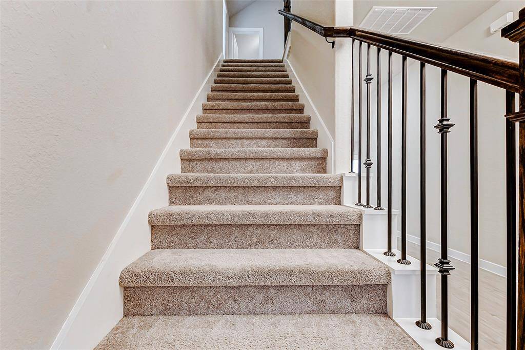 This carpeted staircase with elegant iron spindles leads to the home’s private living quarters upstairs, offering a soft, quiet transition from public to personal space.