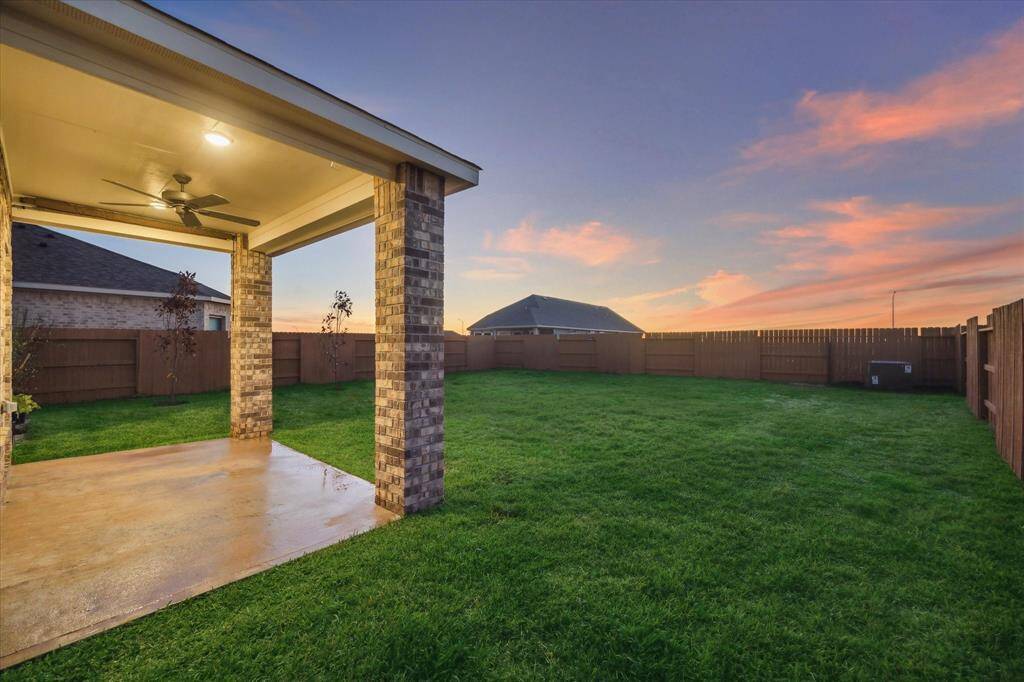 Enjoy serene evenings under this covered patio complete with a ceiling fan, ideal for outdoor dining or relaxation. The expansive green lawn adds to its appeal.