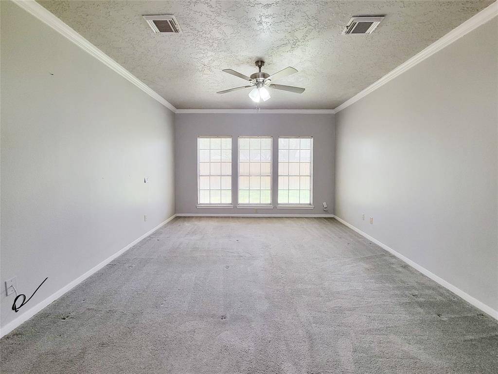 Bright and spacious living room featuring large windows, a ceiling fan, and elegant crown molding. Ideal for relaxation and entertaining.