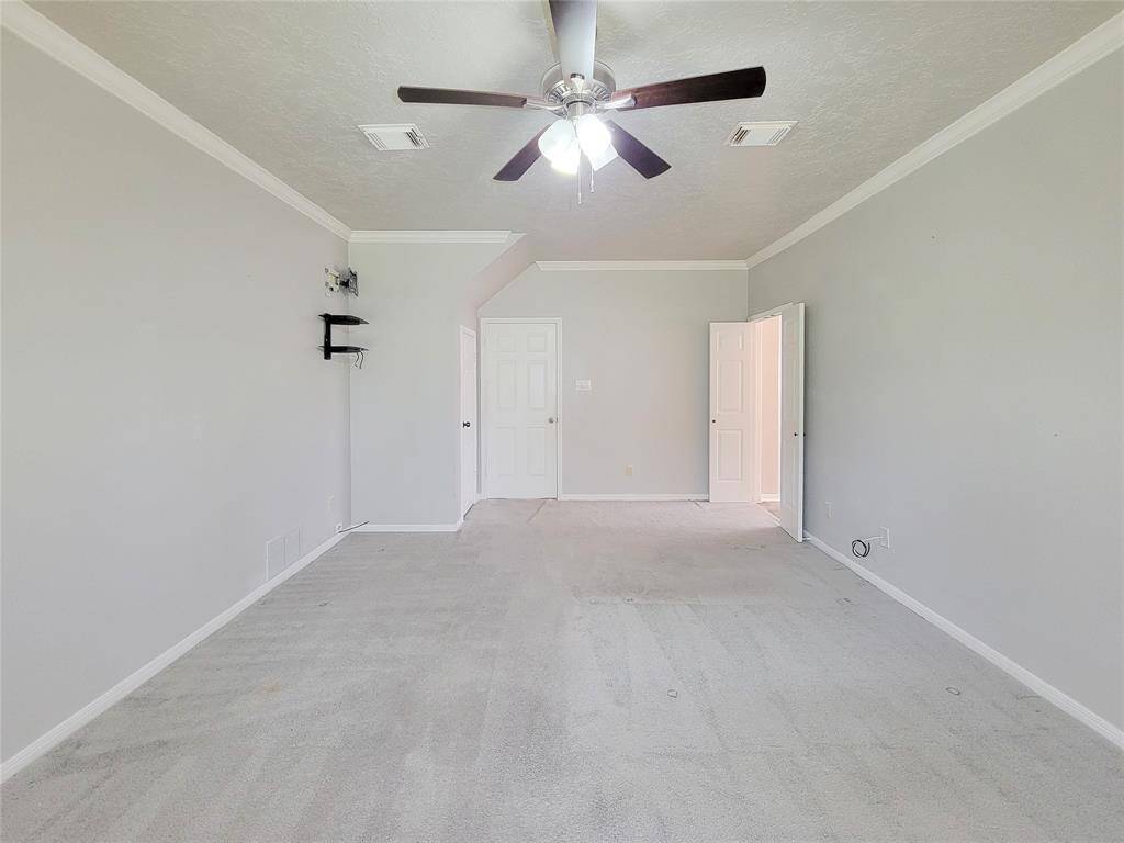 Spacious and bright room with soft carpeting, crown molding, and a modern ceiling fan. Perfect for a cozy retreat or a versatile living space.