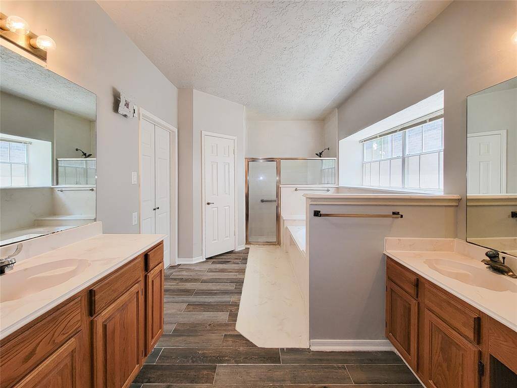 Spacious bathroom with dual sinks, elegant wood cabinetry, and a modern glass-enclosed shower. Natural light floods in through large windows, highlighting the sleek tile flooring and expansive mirrors. Perfect for a relaxing retreat.