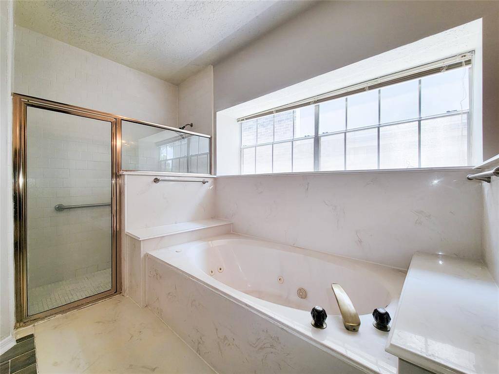 Experience ultimate relaxation in this elegant bathroom featuring a luxurious jetted bathtub and a spacious glass-enclosed shower, all bathed in natural light from the expansive window.