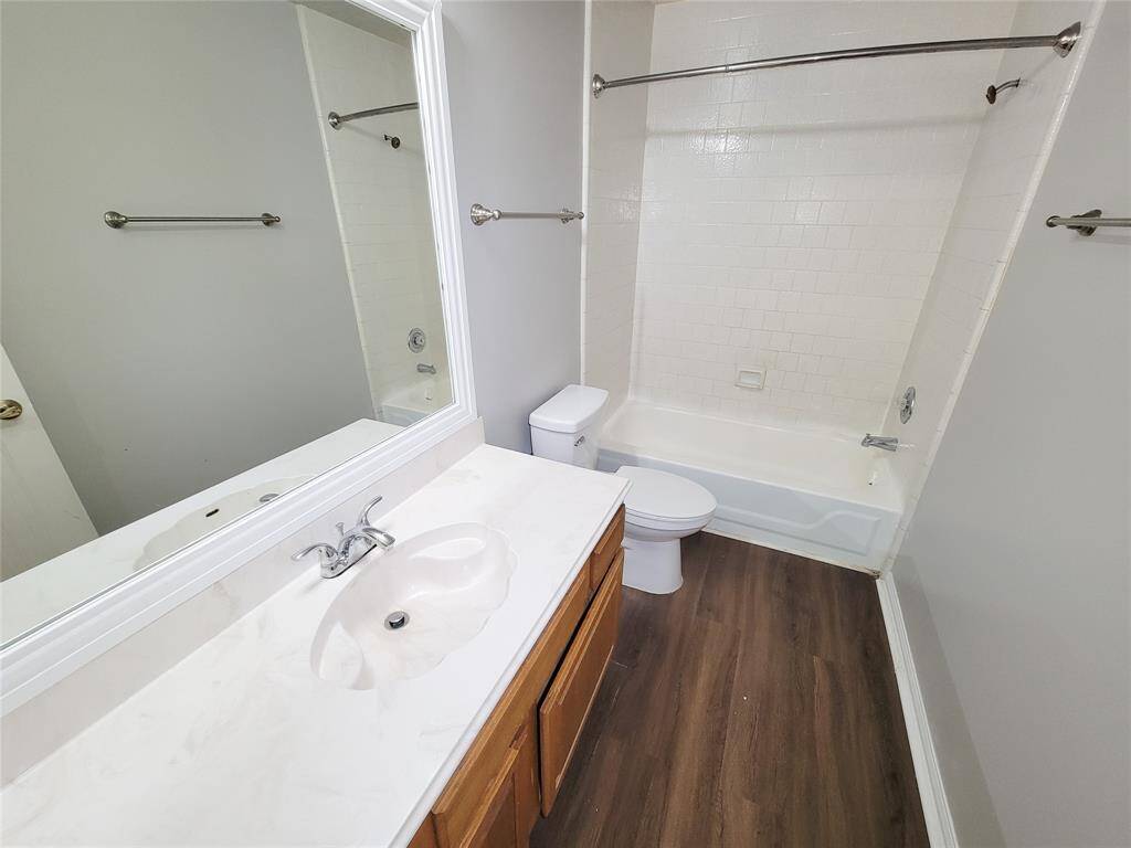 This bright bathroom features a sleek vanity with ample storage, a classic tub-shower combination, and elegant wood flooring, offering both style and functionality.