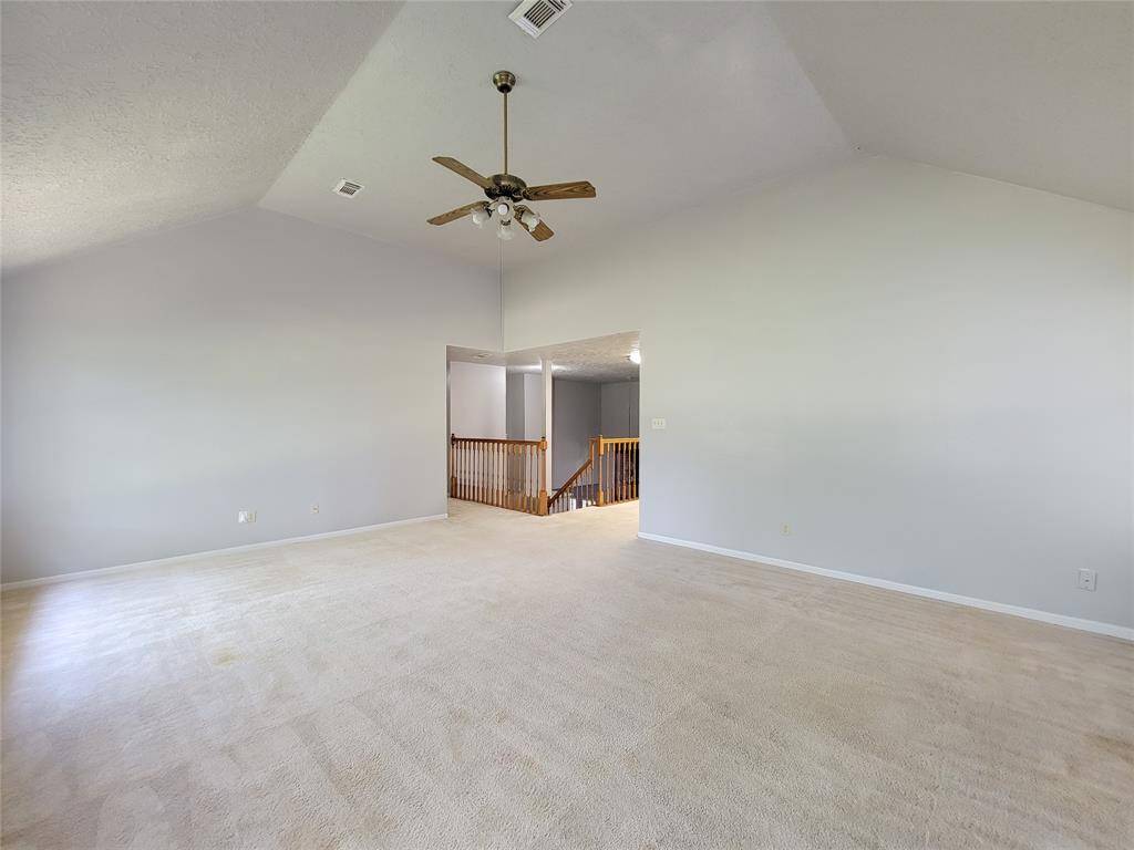 Spacious and bright living area with vaulted ceilings and neutral carpeting, perfect for relaxation and entertaining. Features a ceiling fan and easy access to the upstairs hallway. Ideal for creating your dream space.