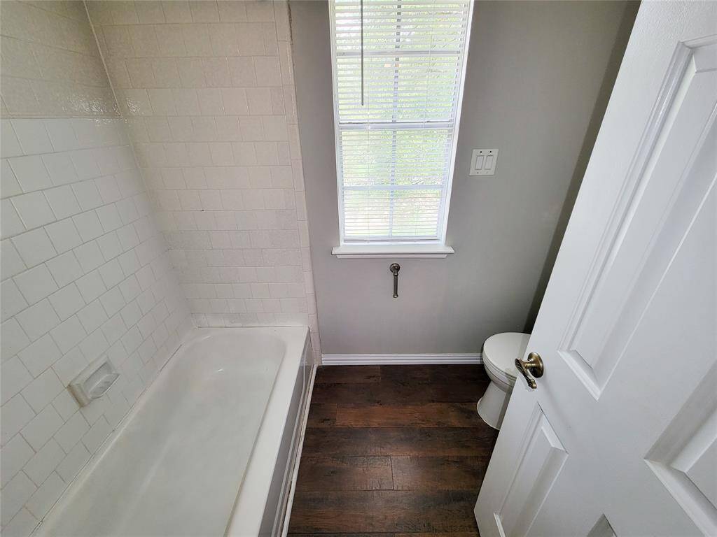 Bright and inviting bathroom featuring a classic white tiled tub, rich hardwood flooring, and a window for natural light. Perfect for relaxation.