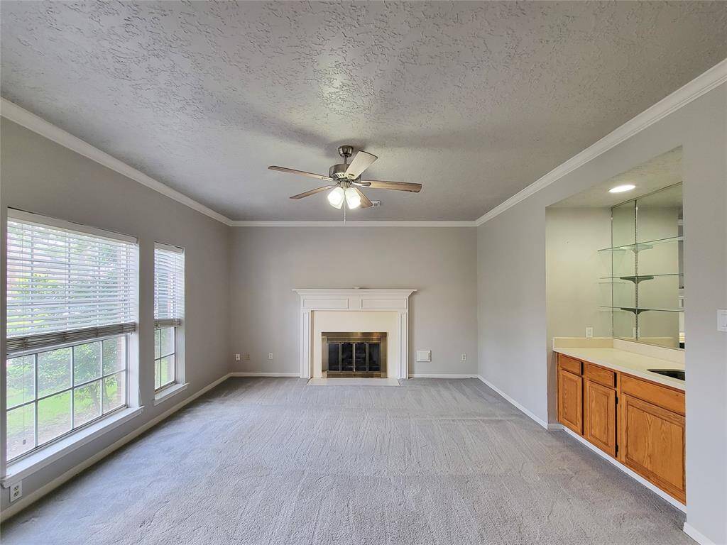 Bright and inviting living room featuring a cozy fireplace, large windows for natural light, and a ceiling fan. Adjacent to a versatile space with built-in shelving, perfect for entertaining.