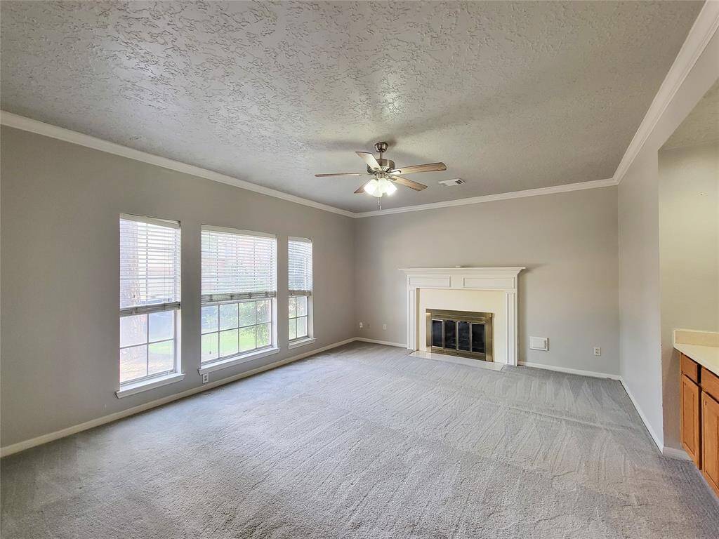 Bright and inviting living room with large windows, a cozy fireplace, and elegant crown molding. Perfect for relaxing or entertaining guests.