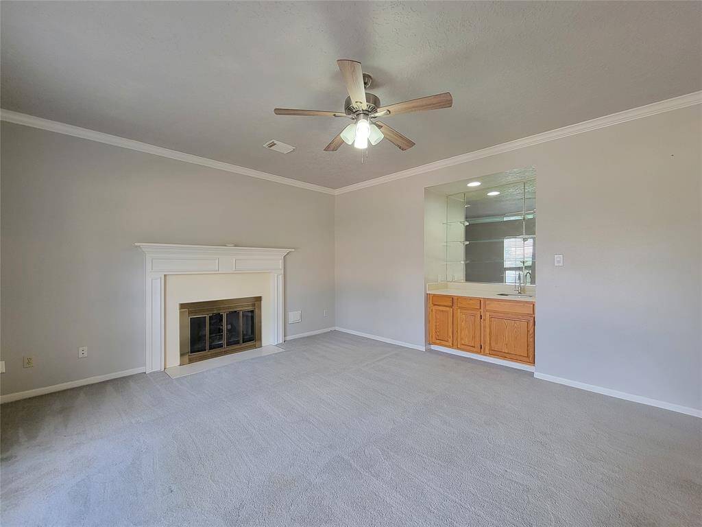 Cozy living room featuring a charming fireplace and built-in wet bar, perfect for entertaining. Neutral tones and a ceiling fan add comfort and style.