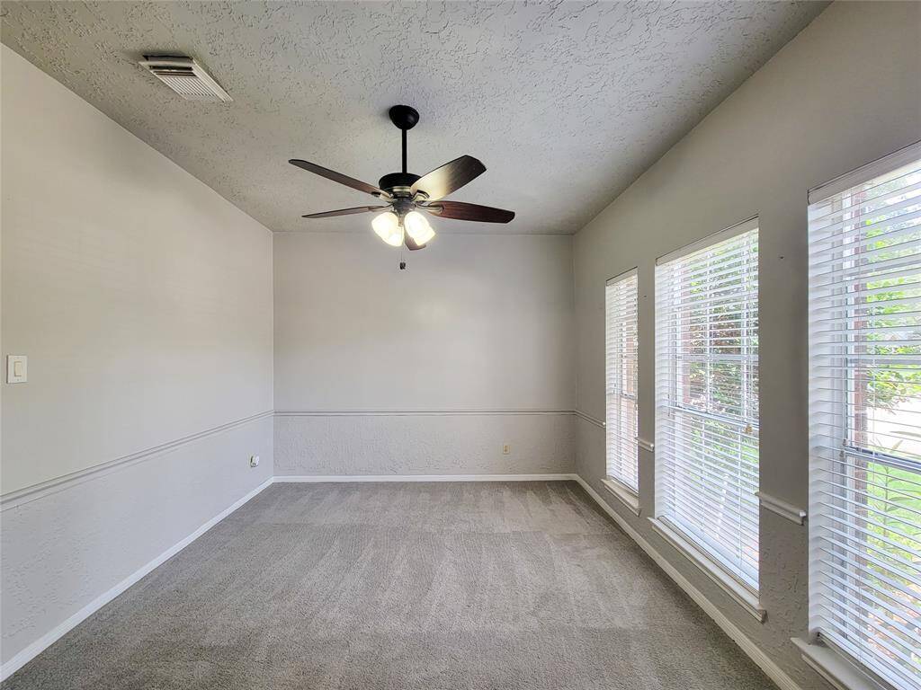 Bright and inviting room with large windows offering abundant natural light. Features include elegant wainscoting, a stylish ceiling fan, and plush carpeting—perfect for a cozy living space or office.
