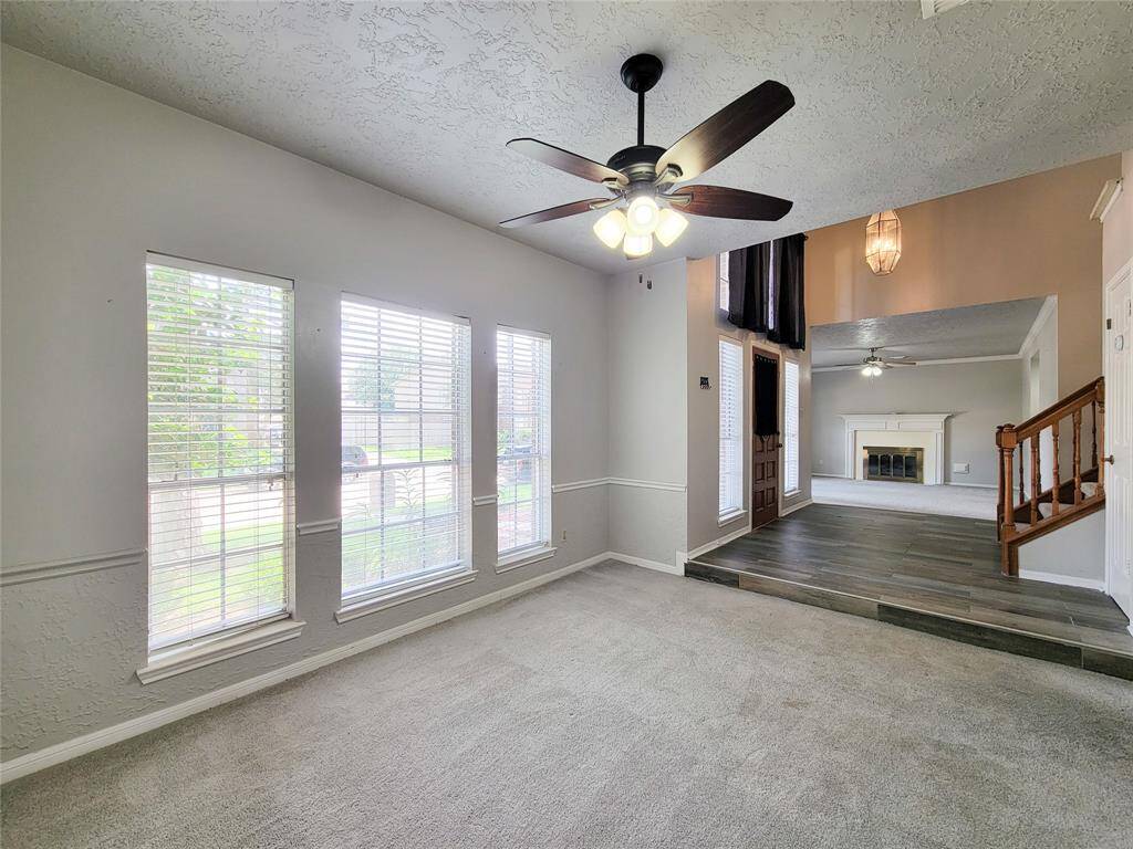 Bright and inviting living space featuring large windows, elegant wainscoting, and a cozy fireplace. The seamless flow between rooms and stylish ceiling fans create a welcoming atmosphere perfect for relaxation and entertaining.