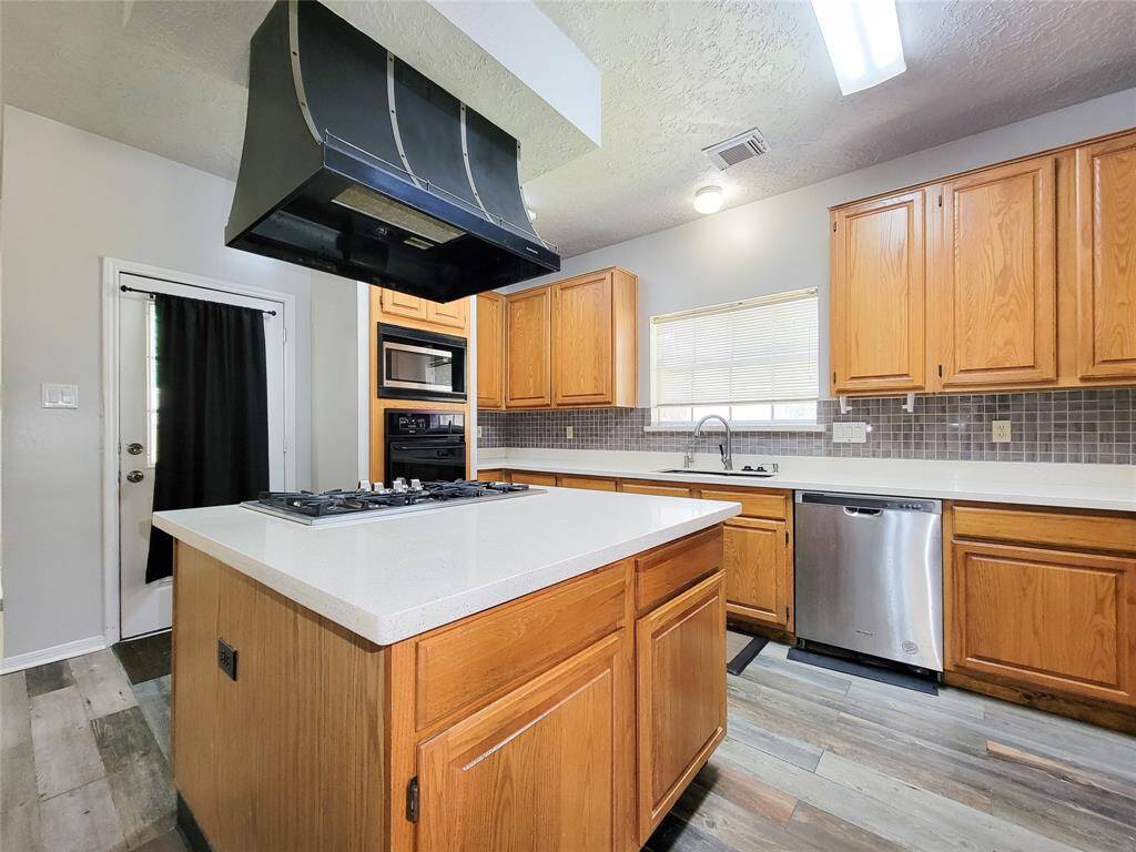 Modern kitchen featuring sleek stainless steel appliances, a spacious island with a built-in stovetop, and ample wooden cabinetry. The updated flooring and abundant natural light create a welcoming atmosphere, perfect for culinary enthusiasts and gatherings.