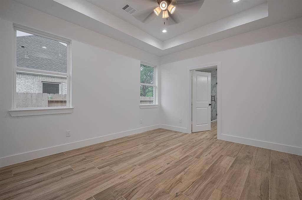 Bright room with wood-look flooring, recessed lighting, and a ceiling fan. Features two windows and an adjacent bathroom with a white door.
