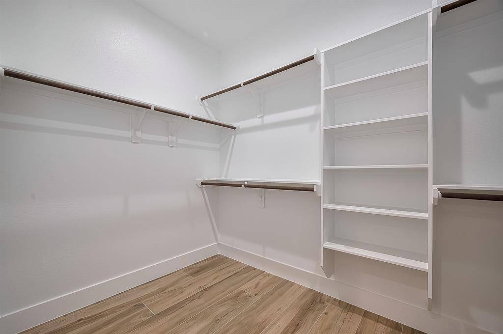 This photo shows a spacious walk-in closet with ample shelving and hanging space, featuring modern wooden flooring and bright white walls for a clean, organized look.