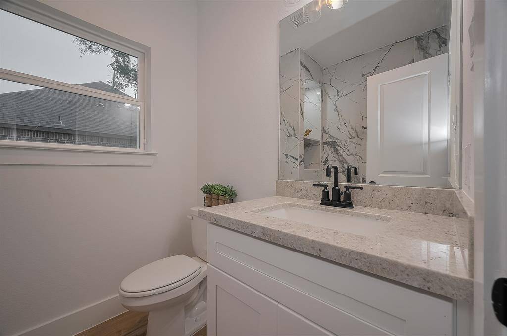 Modern bathroom with a large marble-patterned mirror, sleek white vanity, and black fixtures. It features a window for natural light and a neutral color palette for a fresh, clean look.