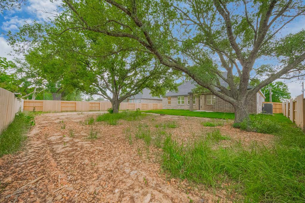 Spacious backyard with mature trees and a well-maintained lawn, surrounded by a wooden fence. Ideal for outdoor activities and privacy.