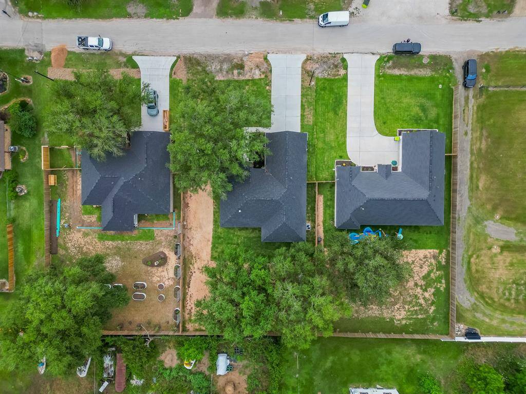 This aerial photo shows three neighboring homes with spacious backyards and driveways. The properties are well-maintained, featuring green lawns and some mature trees. The layout provides a sense of privacy and ample outdoor space for activities.