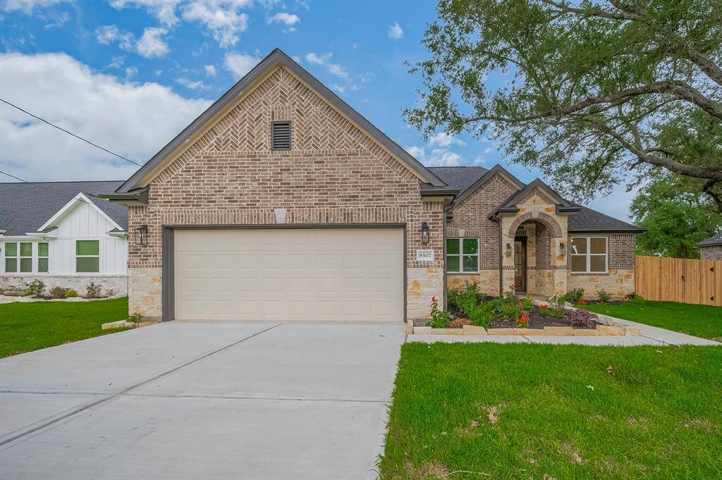 Charming single-story home with a brick exterior and a spacious two-car garage. The front yard is well-maintained, featuring a neat lawn and vibrant flower beds. An inviting arched entryway adds character to this attractive property.