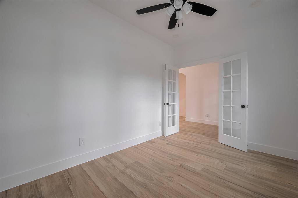 Bright room with light wood flooring, white walls, and a ceiling fan. Features French doors leading to another space, enhancing the open feel.