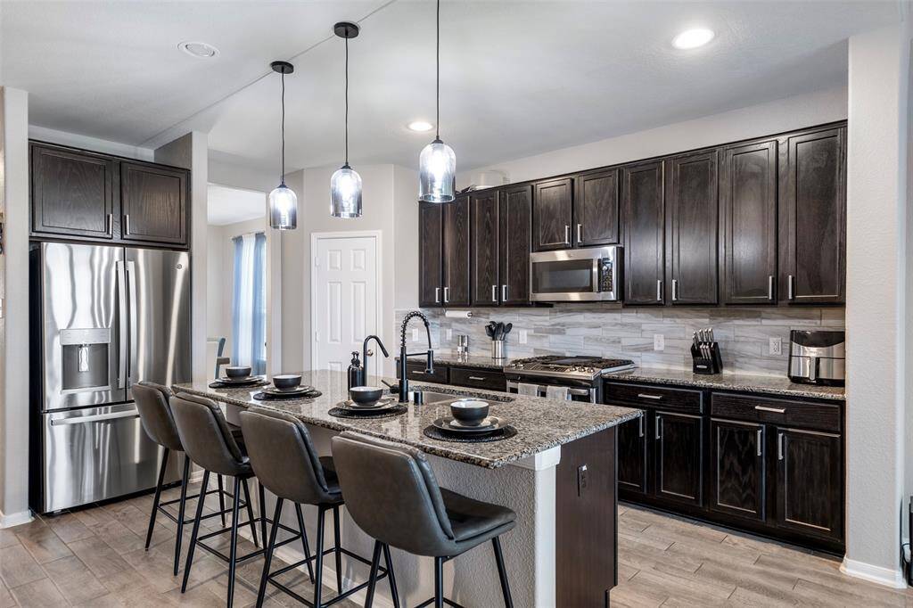 This modern kitchen features sleek dark wood cabinets, stainless steel appliances, and a spacious island with seating for four. The pendant lighting adds a stylish touch, and the open layout is perfect for entertaining.
