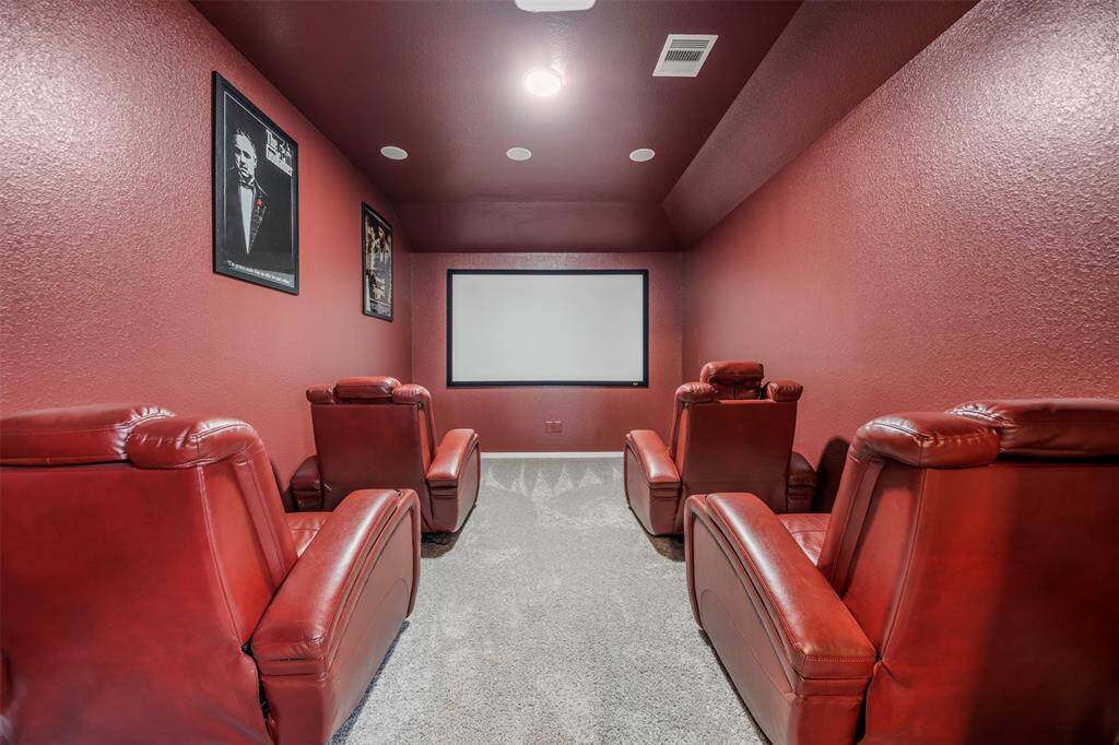 This photo showcases a cozy home theater room featuring four plush red recliners, a large screen, and rich red walls with decorative posters. Ideal for movie nights, the space combines comfort with style in a dedicated entertainment setting.