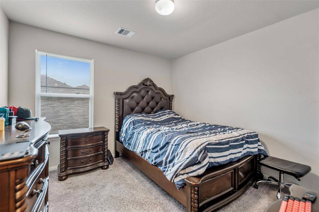 This cozy bedroom features a large window for natural light, a plush carpet, and elegant dark wood furniture, including a bed with a tufted headboard and matching dresser.