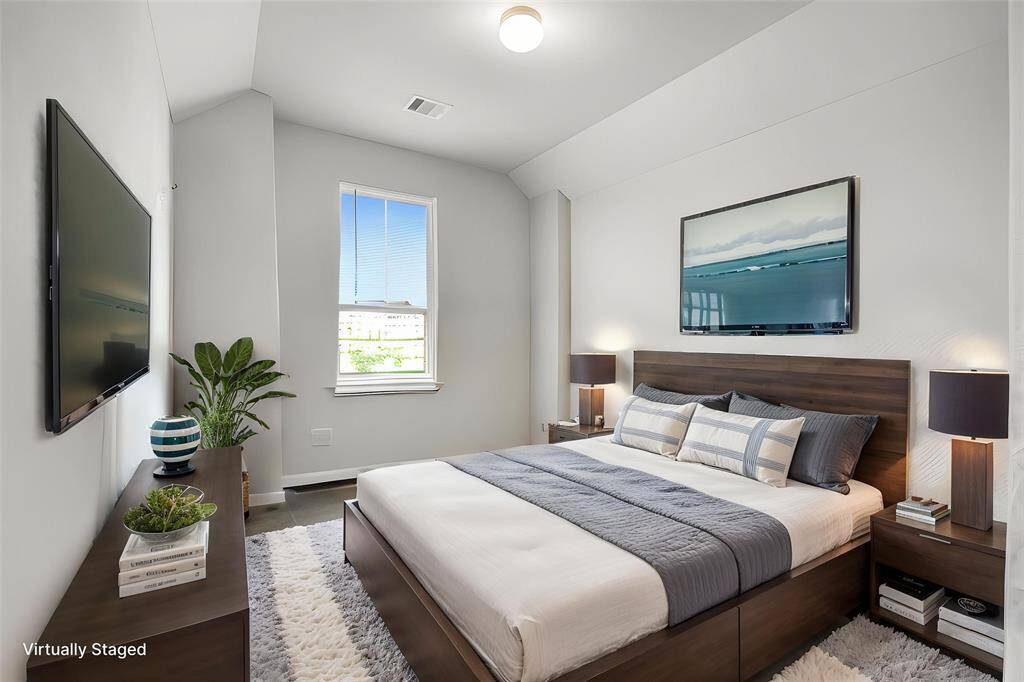 This is a modern, virtually staged bedroom featuring a comfortable bed with neutral bedding, a mounted flat-screen TV, and stylish decor. The room has a large window allowing natural light, a plush rug, and elegant lighting, creating a cozy and inviting atmosphere.