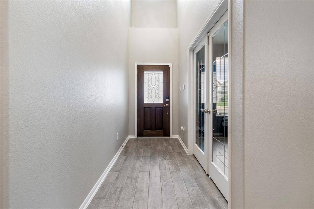 Bright and welcoming entryway with light-colored walls and wood-look flooring. Features a front door with decorative glass and adjacent French doors leading to another room, creating an inviting first impression.
