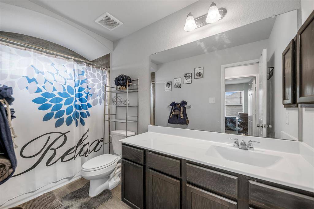 This modern bathroom features a large mirror, dual sinks with dark wood cabinetry, and a relaxing shower area with a stylish curtain. It has ample natural light and tasteful decor, making it both functional and inviting.