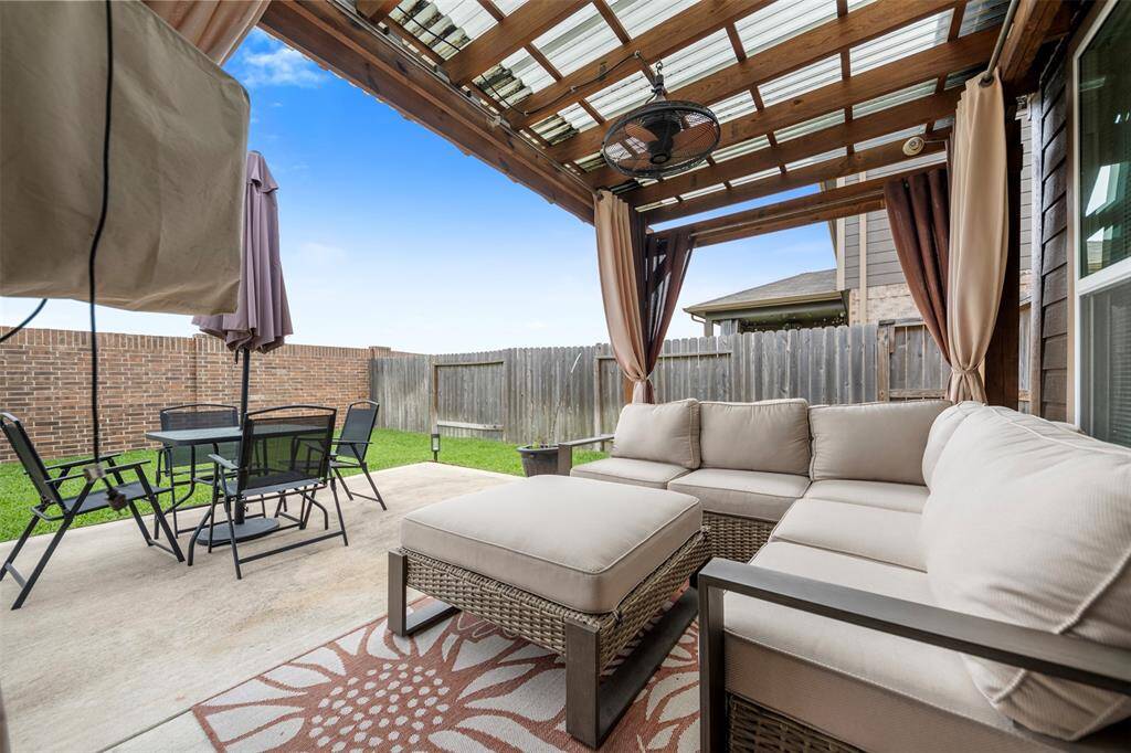 This photo showcases a cozy backyard patio with a pergola, featuring comfortable seating, a ceiling fan, and a dining area. The space is perfect for relaxation and outdoor gatherings, with a fenced yard for added privacy.