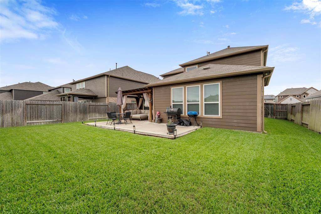 This photo showcases a spacious backyard with a well-maintained lawn, a patio area for outdoor dining, and a privacy fence, perfect for relaxation and entertainment.
