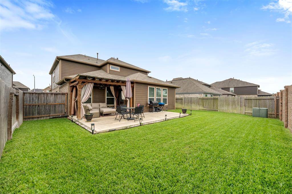 This backyard features a well-maintained lawn and a spacious patio with a pergola, providing an ideal space for outdoor relaxation and entertaining. The area is fenced for privacy.