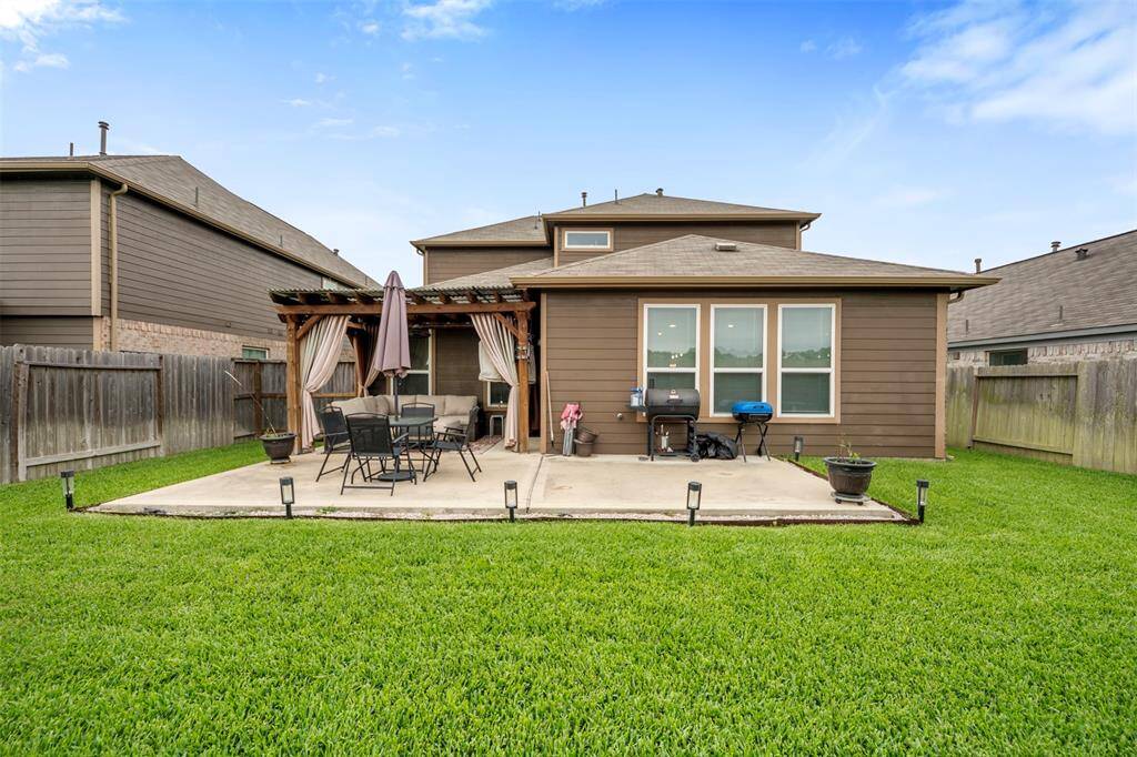 This photo showcases a backyard with a well-maintained lawn, a concrete patio, and a pergola with outdoor seating and a grill, ideal for entertaining or relaxing.