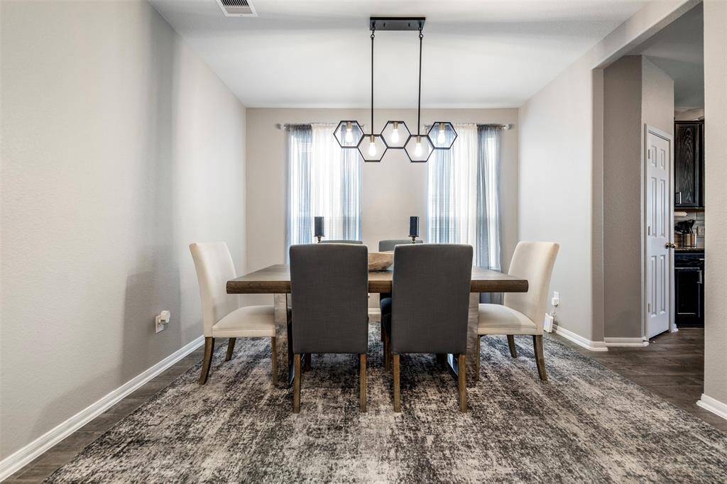 This dining room features a modern design with a sleek, wooden table and a mix of upholstered chairs. A geometric chandelier adds a stylish touch, and natural light filters through sheer curtains, creating a bright and inviting space.