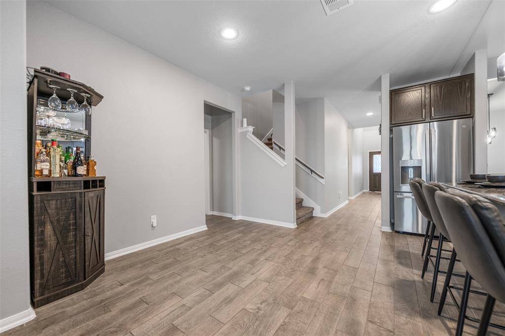 This modern home features an open layout with sleek wood-look flooring, a stylish dry bar, and a contemporary kitchen with stainless steel appliances. The hallway leads to a staircase, enhancing the spacious feel. Perfect for entertaining and comfortable living.