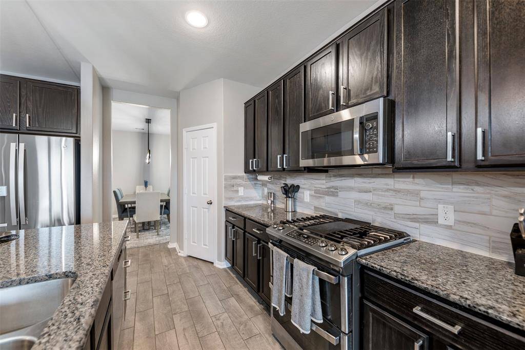This modern kitchen features dark wood cabinets, stainless steel appliances, and granite countertops. The space is bright with recessed lighting and opens to a dining area, offering a sleek and functional design.