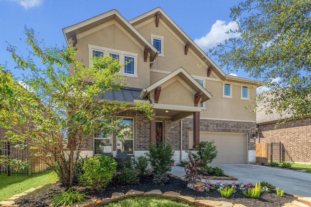 This charming two-story home features a modern farmhouse design with a mix of brick and siding exterior. It includes a covered front porch, a well-maintained front yard with landscaped beds, shrubs, and a spacious driveway leading to a two-car garage. The roof has gabled accents adding character to the facade.