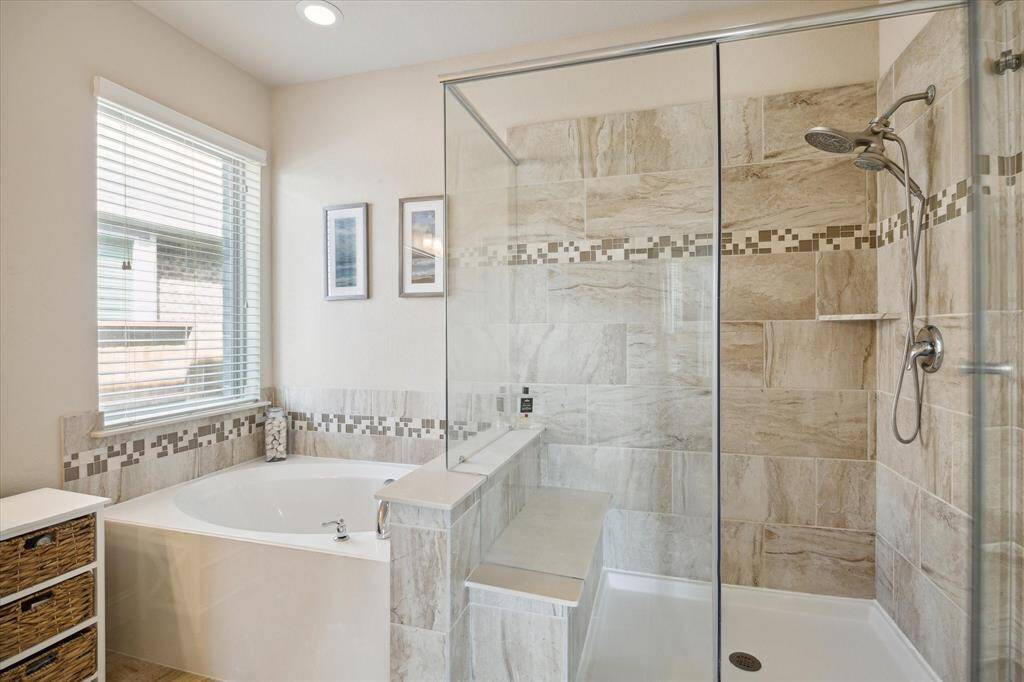 This bathroom features a modern design with a large glass-enclosed shower, a separate soaking tub, and stylish tile work. Updated to current trends and lots of storage and counter space. Natural light streams in through a window, enhancing the bright and airy feel.
