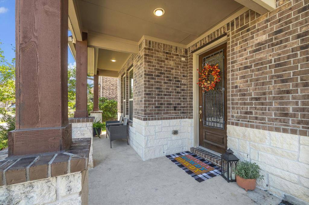 Generous front entrance features rustic pillars, brick and stone facade with a decorative front door and a cozy seating area on the covered porch, ideal for relaxation and waving to the neighbors.