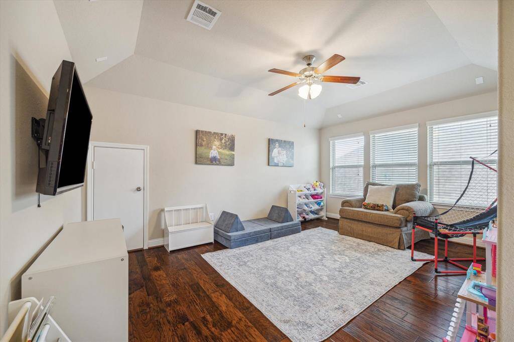 Bright playroom with hardwood floors, featuring a ceiling fan, large windows, and ample space for toys and seating.