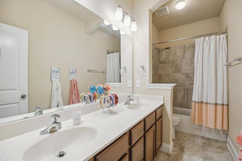 This bathroom features a double vanity with sleek fixtures, a large mirror, and ample storage. It includes a combined shower and bathtub with elegant tile work, complemented by warm lighting and a neutral color palette.
