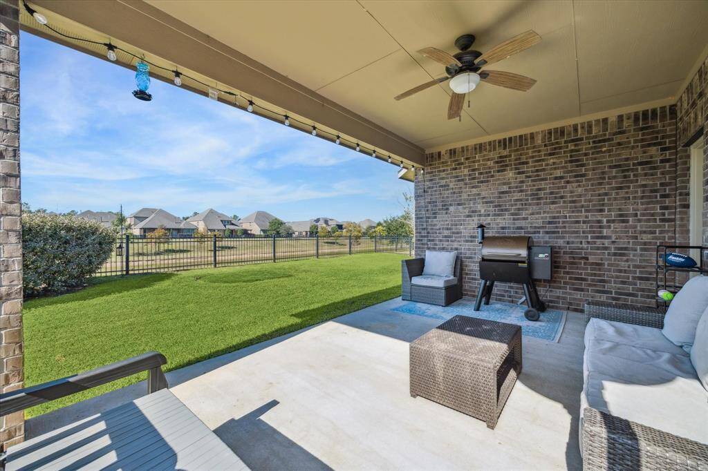 Spacious covered patio with comfortable seating, ceiling fan, and grill, overlooking a well-maintained backyard with a scenic view of neighboring houses. Perfect for outdoor relaxation and entertaining.