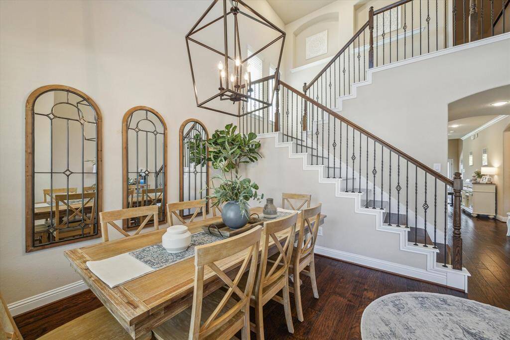 This photo showcases a dining area looking into the first floor living and stylish staircase with wrought iron railings and double height ceilings.