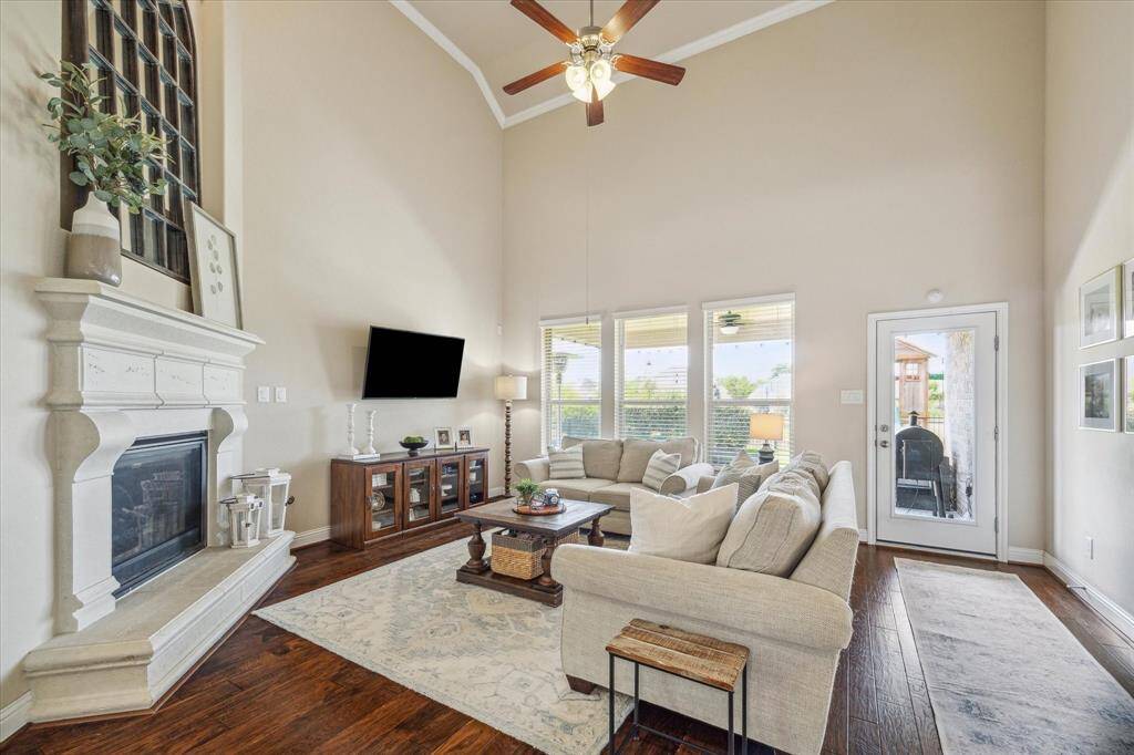 This spacious living room features high ceilings, a cozy fireplace, and abundant natural light from large windows.  Door to the backyard and covered patio.  Wood flooring, and a ceiling fan, creating a welcoming room for family and friends.