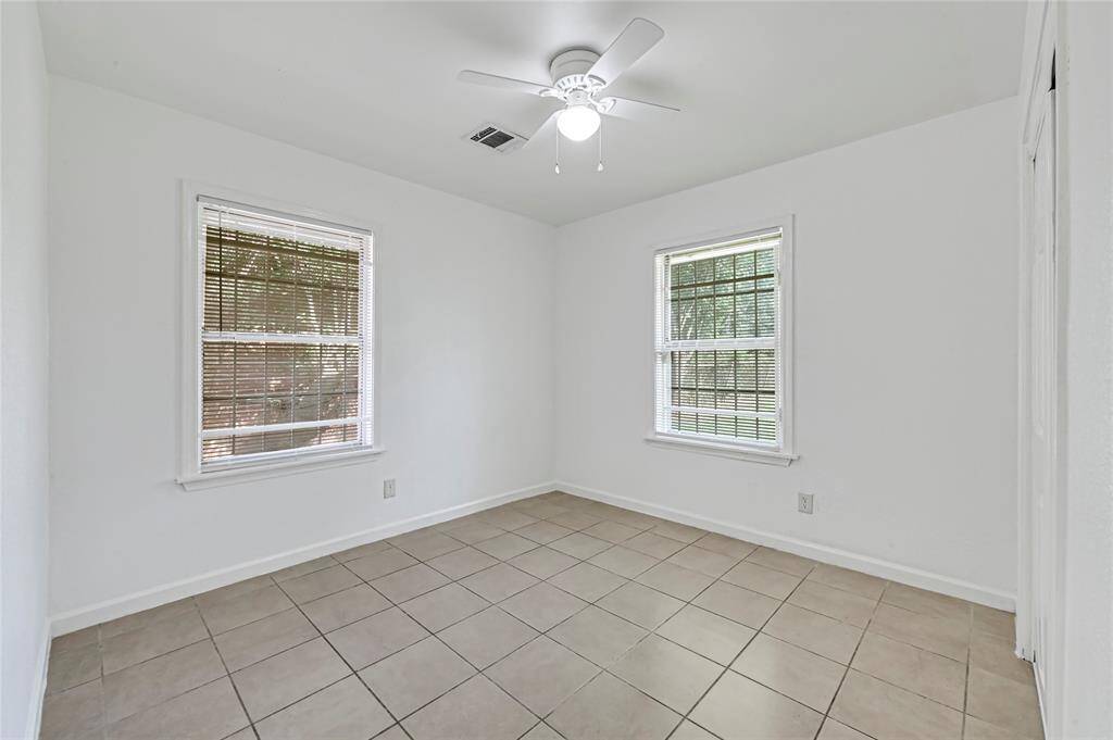 This bedrom features neutral tile flooring, two windows with blinds, and a ceiling fan. Perfect for an office or guest room.