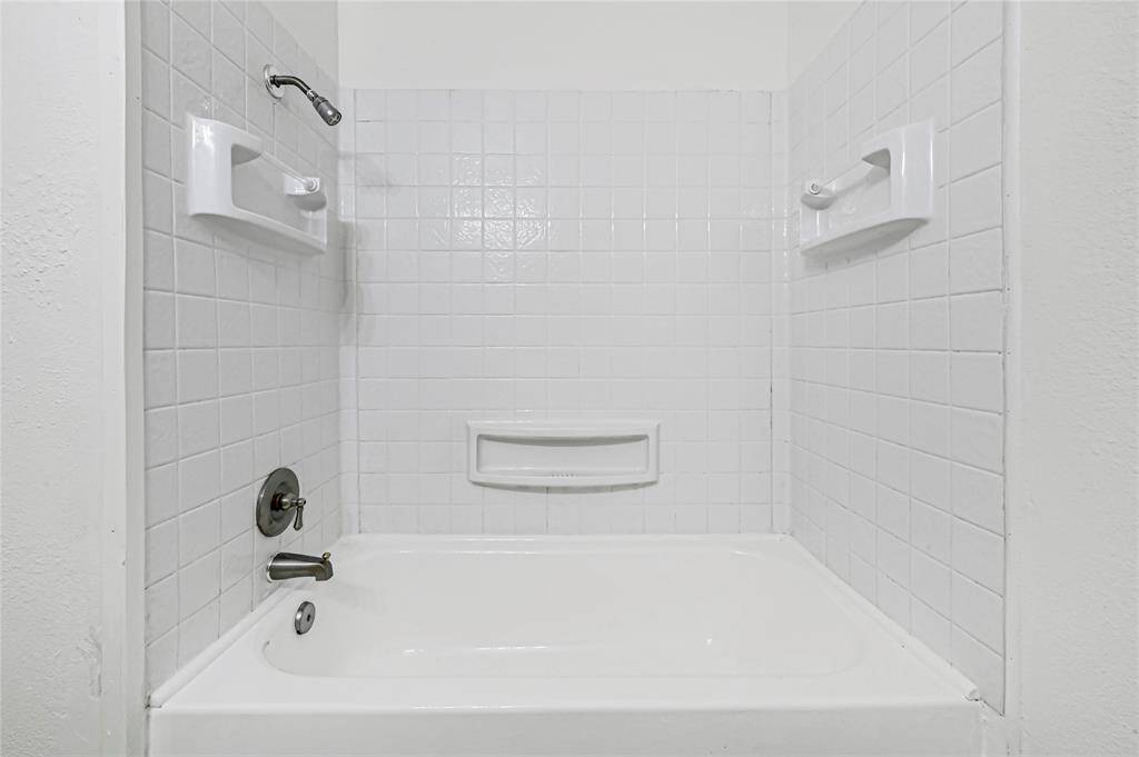 This is home is move-in ready with a tub and shower combination, featuring classic white tile walls and built-in soap holders.