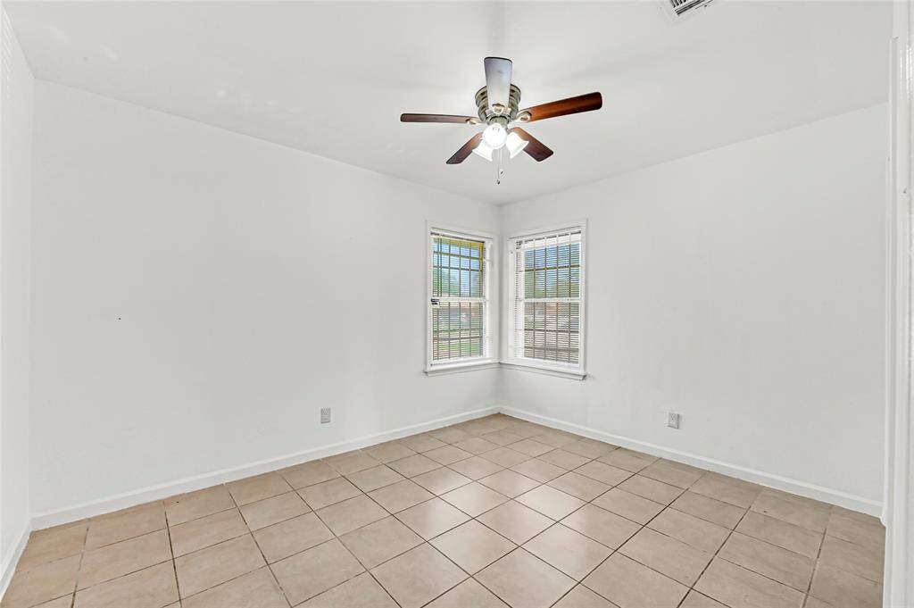 Bright, minimalist room with tiled floors and white walls. Features a ceiling fan and two large windows providing ample natural light. Ideal for a cozy bedroom or office space.