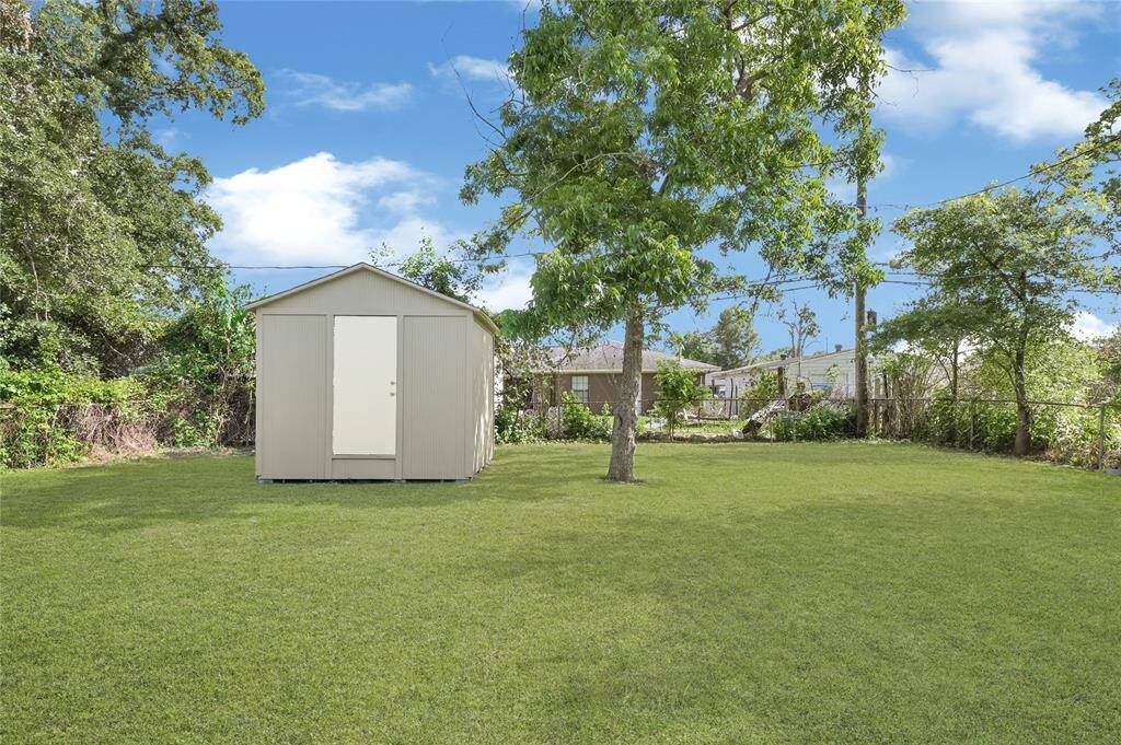 Spacious backyard with a well-maintained lawn, featuring a storage shed and mature trees for shade and privacy. Ideal for outdoor activities and gardening.