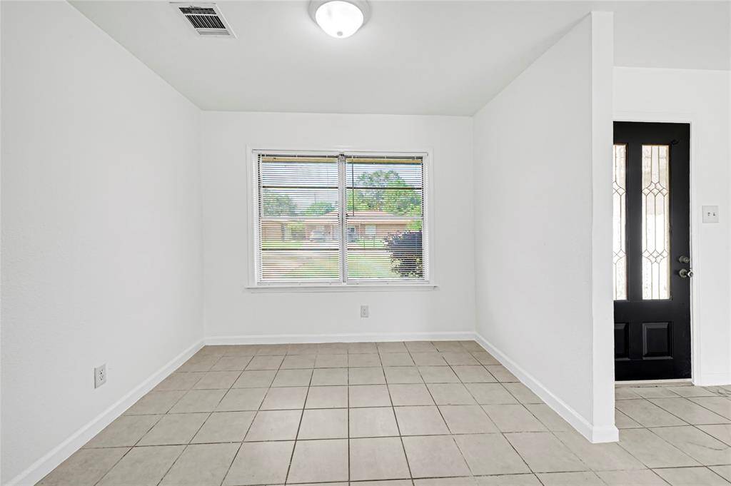 Bright and welcoming entryway with tiled flooring, neutral walls, and a modern black front door. A large window offers natural light and a view of the front yard.