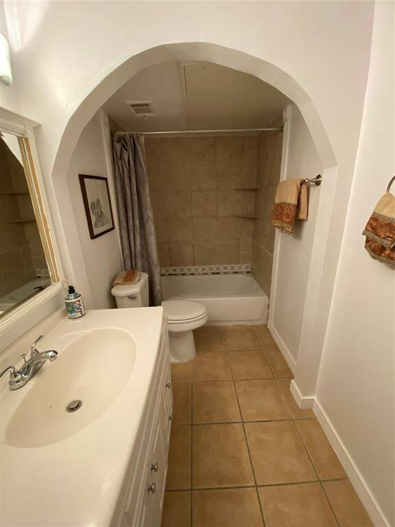 This bathroom features a tiled floor and a alcove with a bathtub and shower. It includes a vanity with a sink, a toilet, and a towel rack, providing a functional and inviting space.